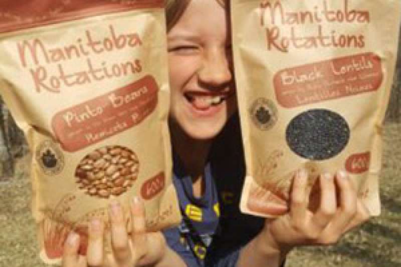 A child smiles as they hold up two bags of Adagio Acres legumes on either side of their face.