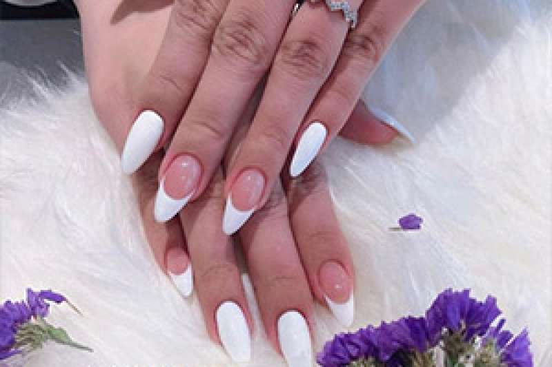 A beautifully manicured pair of hands against a fluffy white background surrounded by small purple flowers.
